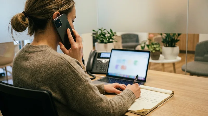 Dental office manager calling the practice line from a mobile phone while checking notes at a desk