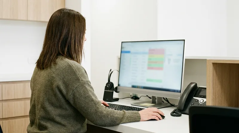 Dental office manager reviewing an overdue recall report flagging at-risk patients on a front desk monitor