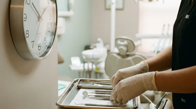 Dental assistant preparing an operatory tray beside a clock, illustrating measured chair time for each appointment type