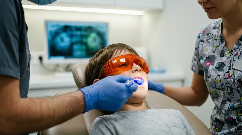 Dentist using a blue curing light to harden a sealant on a calm boy's back tooth
