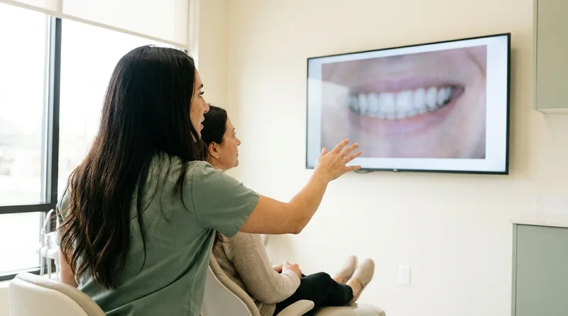 A dentist showing a patient a digital smile preview on a monitor during a consultation